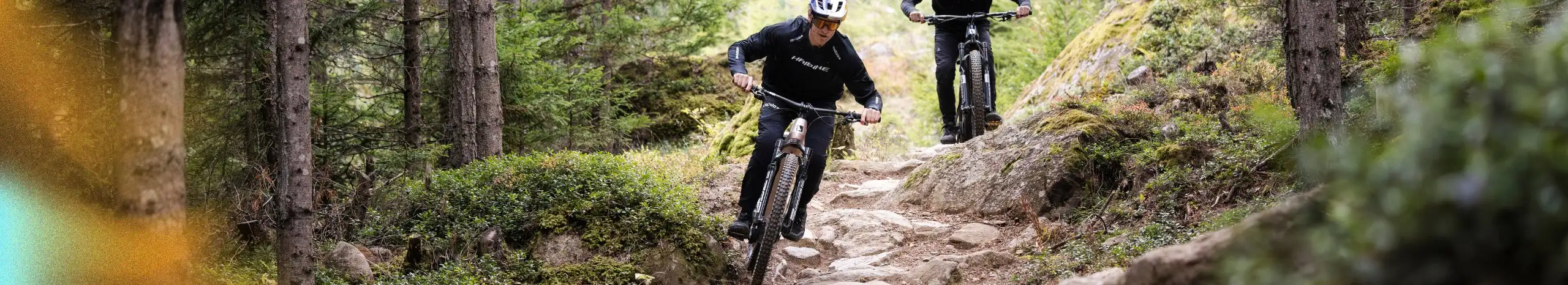 Kaksi sähköpyöräilijää maastojja ajamassa kivikkoa kovaa alaspäin. Haibike sähköpyörät kuvassa.