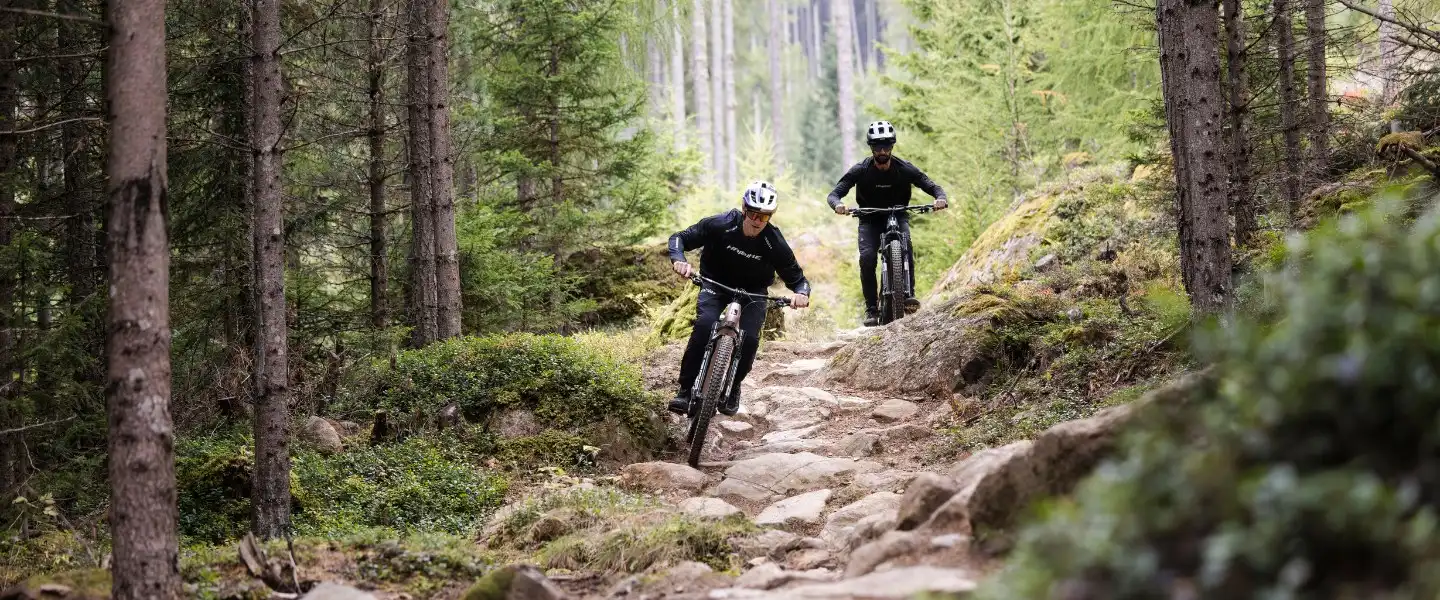 Kaksi sähköpyöräilijää maastojja ajamassa kivikkoa kovaa alaspäin. Haibike sähköpyörät kuvassa.